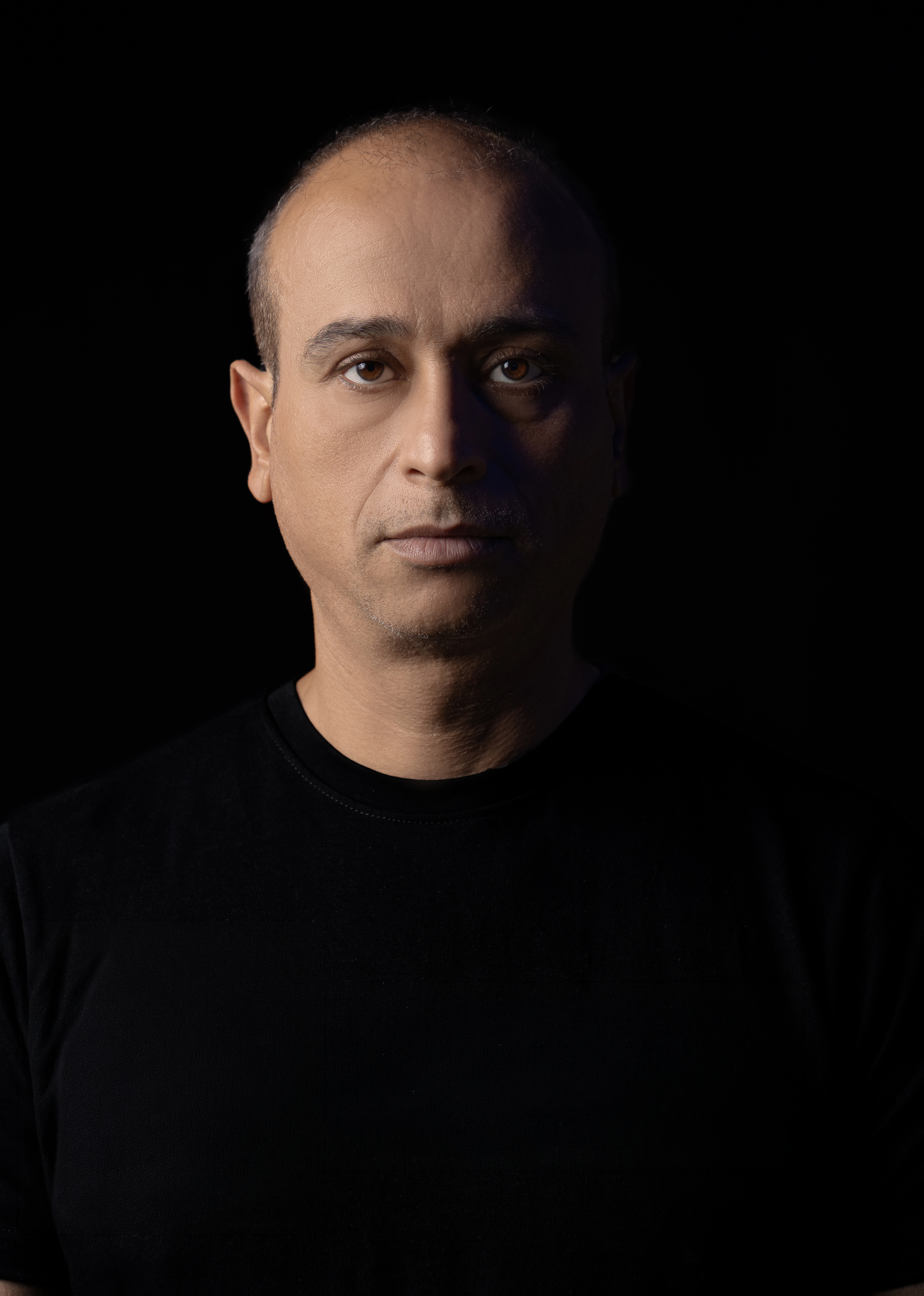 Omer pictured in a black shirt against a dark background.